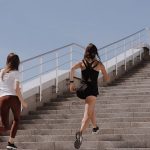 Two women running up stairs outdoors, embodying fitness and wellness.
